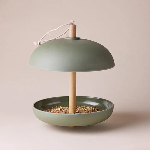 Green bird feeder with wooden perch on a beige background