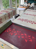 Image shows oatmeal coloured  Irish Linen tea towel with red floral print in production.