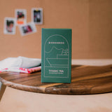 Green box labeled 'Born & Bred Titanic Tea' on a wooden surface with blurred background