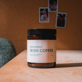 Jar Candle of BornBred Irish Coffee Scent on a wooden surface with a warm-toned wall in the background.