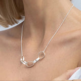 Silver necklace worn by a person with a plain background
